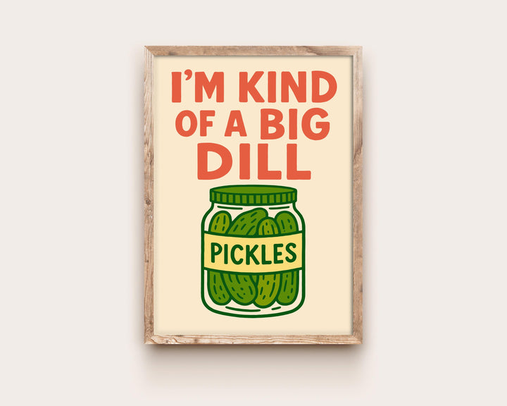 May include: A framed print featuring the phrase "I'M KIND OF A BIG DILL" in red, above a cartoon jar of pickles. The jar is green with a yellow label reading "PICKLES". The background is a light beige colour.